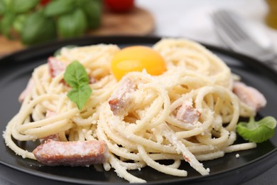 Photo of Tasty pasta Carbonara with basil leaves and egg yolk on plate, closeup