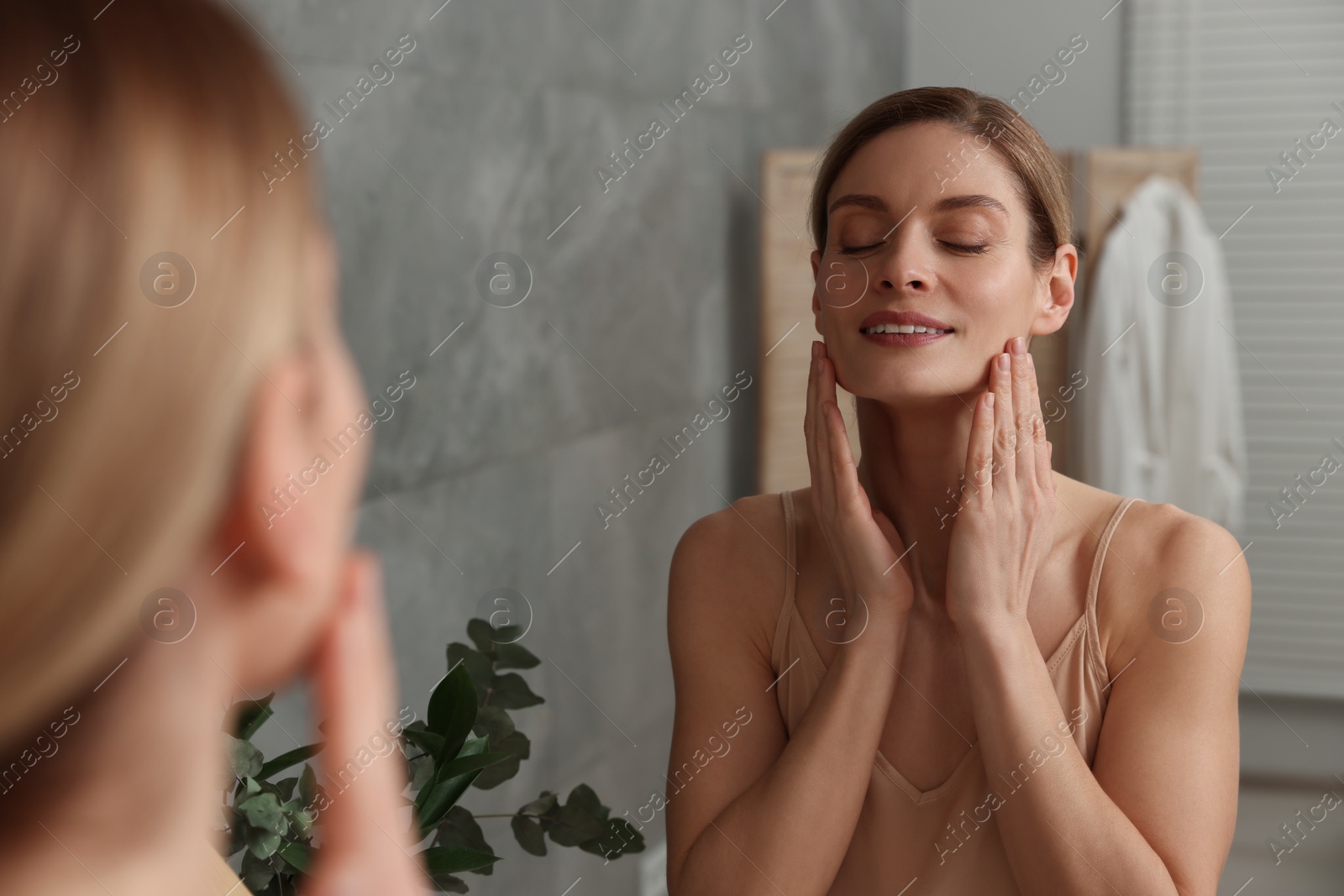 Photo of Woman massaging her face near mirror in bathroom
