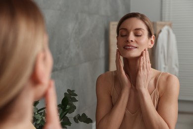 Woman massaging her face near mirror in bathroom