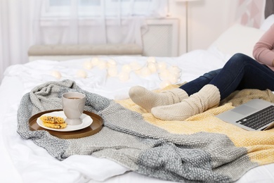 Photo of Woman with cup of hot drink and wafers on bed at home. Cozy winter