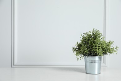 Aromatic green potted rosemary on wooden table near white wall, space for text