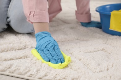 Woman in rubber gloves cleaning carpet with rag, closeup. Space for text