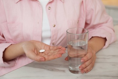 Photo of Young woman with abortion pill and glass of water at white marble table, closeup