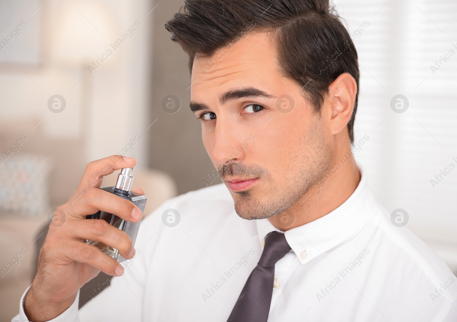 Photo of Handsome young man using luxury perfume indoors