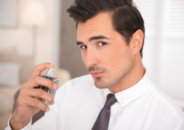 Handsome young man using luxury perfume indoors