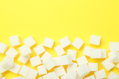Photo of White sugar cubes on yellow background, top view. Space for text