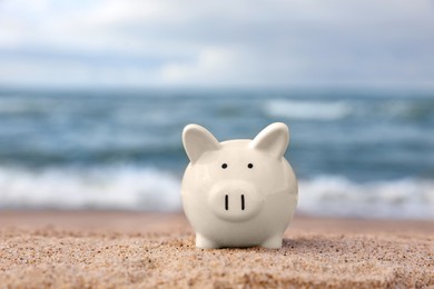 Cute piggy bank on sand near sea