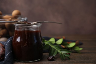 Jar of tasty tamarind sauce, spoon and fresh pods on wooden table. Space for text