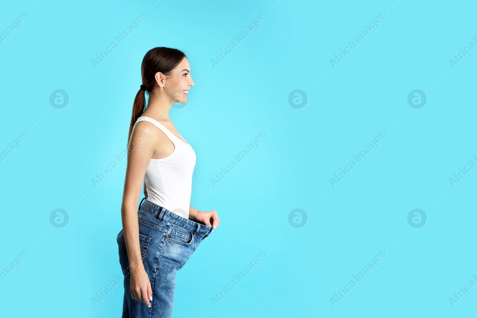 Photo of Attractive young woman with slim body wearing her old big jeans on color background. Space for text