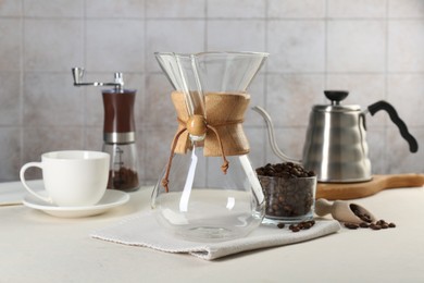 Photo of Empty glass chemex coffeemaker with and beans on white table