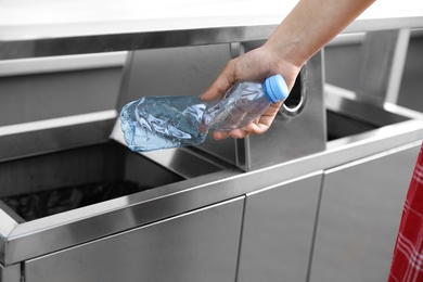 Photo of Woman throwing plastic bottle into recycling bin outdoors, closeup