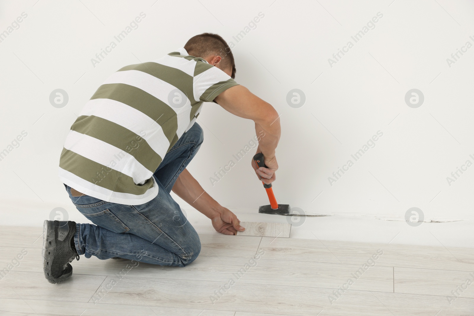 Photo of Professional worker using hammer during installation of new laminate flooring indoors