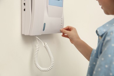 Photo of Cute little girl pressing button on intercom panel indoors, closeup