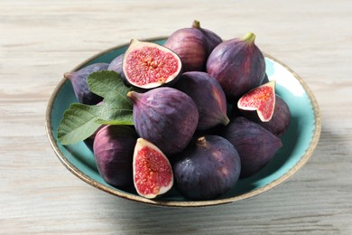 Photo of Plate with fresh ripe figs and green leaf on white wooden table, closeup