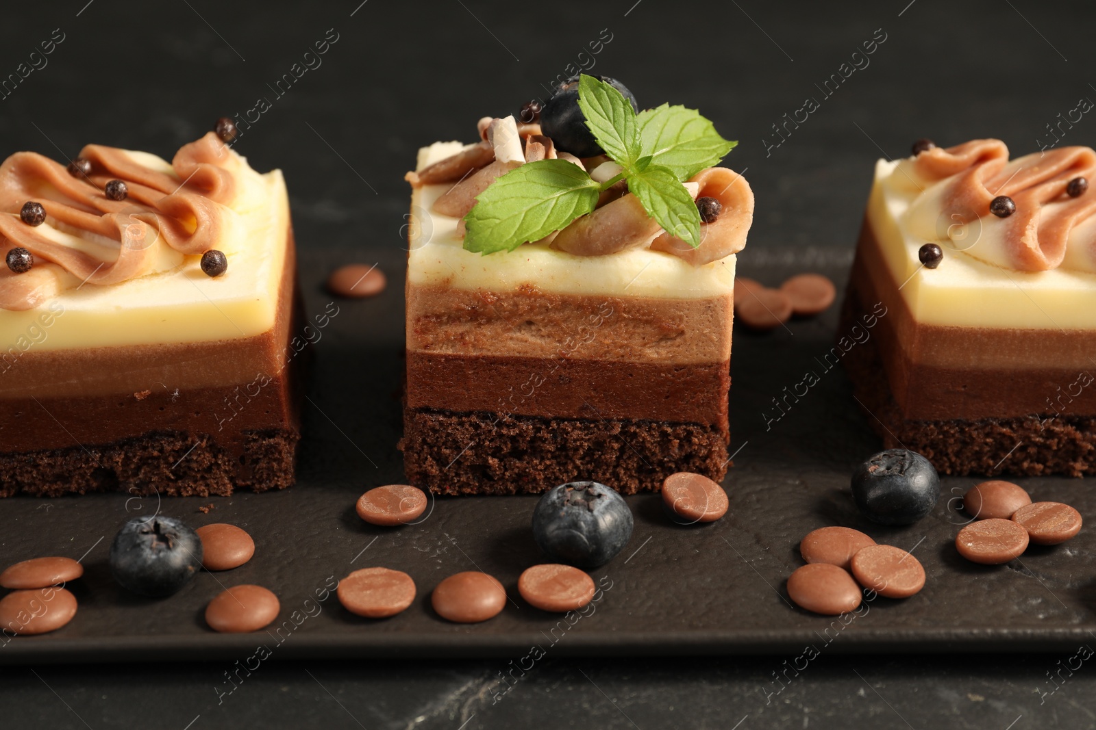 Photo of Pieces of triple chocolate mousse cake on black table, closeup