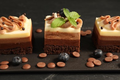 Photo of Pieces of triple chocolate mousse cake on black table, closeup