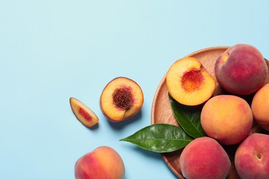 Cut and whole fresh ripe peaches with green leaves on light blue background, flat lay. Space for text