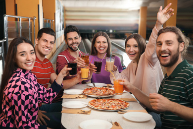 Group of friends with drinks and pizza in bowling club