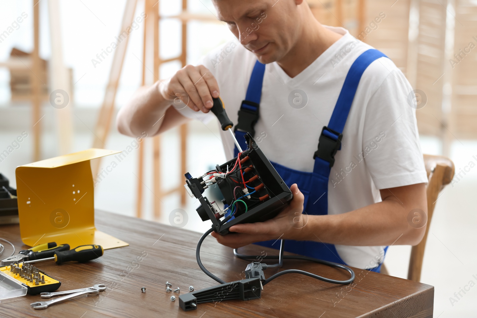 Photo of Professional technician repairing electric fan heater with screwdriver at table indoors