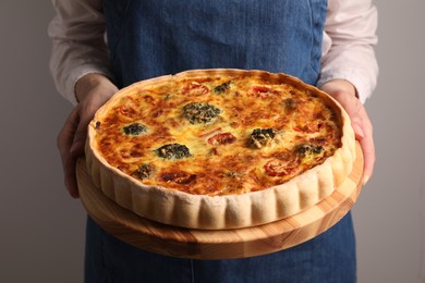 Woman holding delicious homemade vegetable quiche on light gray background, closeup