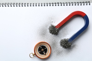 Photo of Compass and magnet with iron powder on notebook, top view. Space for text