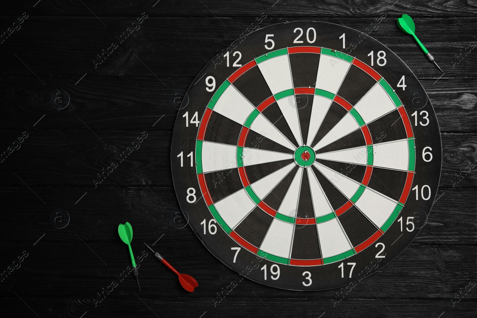 Photo of Dart board with color arrows on black wooden background, top view