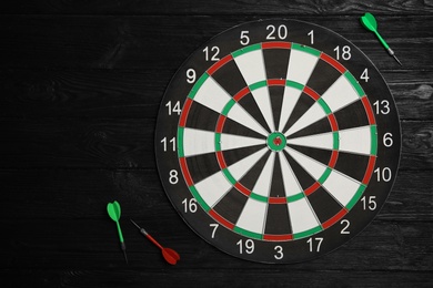 Photo of Dart board with color arrows on black wooden background, top view