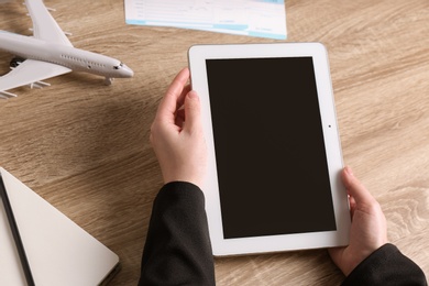 Photo of Woman holding tablet with blank screen over table, closeup. Travel agency