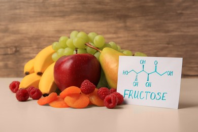 Photo of Card with word Fructose, delicious ripe fruits, raspberries and dried apricots on beige table