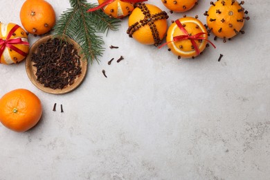 Pomander balls made of tangerines with cloves and fir branch on grey table, flat lay. Space for text