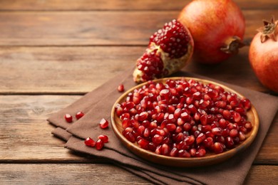 Photo of Ripe juicy pomegranates and grains on wooden table. Space for text