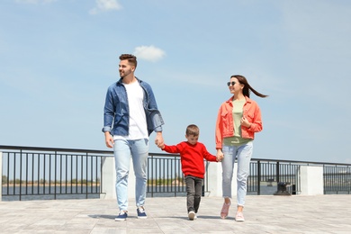 Photo of Happy child holding hands with his parents outdoors. Family weekend