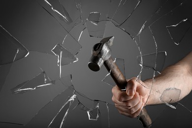 Image of Man breaking window with hammer on dark grey background, closeup