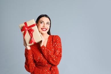 Woman in red dress holding Christmas gift on grey background, space for text