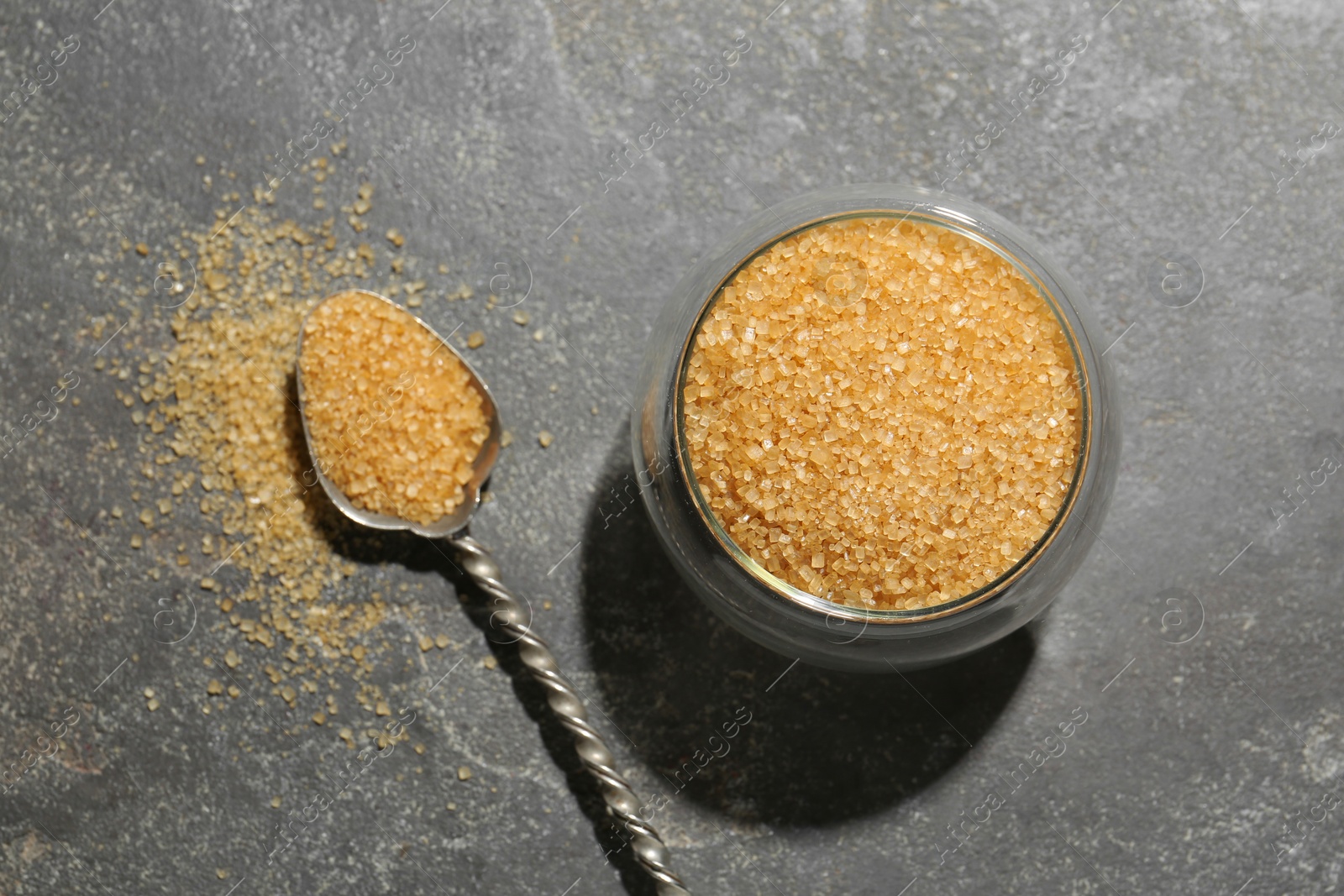 Photo of Brown sugar in bowl and spoon on grey textured table, top view