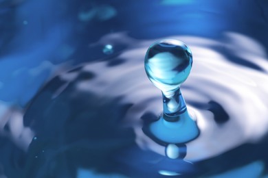 Photo of Splash of clear water with drop on blue background, closeup