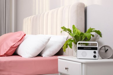 Photo of Stylish radio receiver, plant and clock on nightstand in bedroom