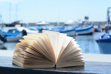 Photo of Open book on wooden bench near sea
