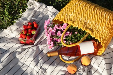 Yellow wicker bag with beautiful flowers, bottle of wine and food on picnic blanket outdoors