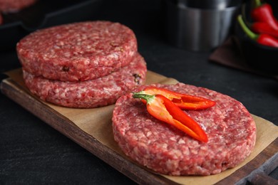 Photo of Raw hamburger patties with chili pepper on black table, closeup