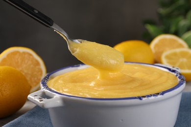 Photo of Taking delicious lemon curd from bowl at table, closeup