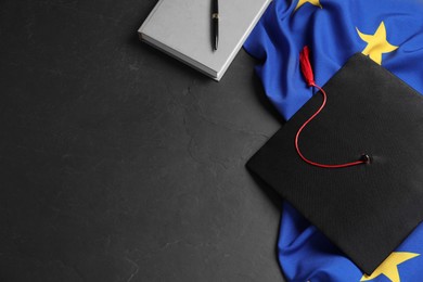 Photo of Graduation cap, book, pen and flag of European Union on black table, flat lay. Space for text