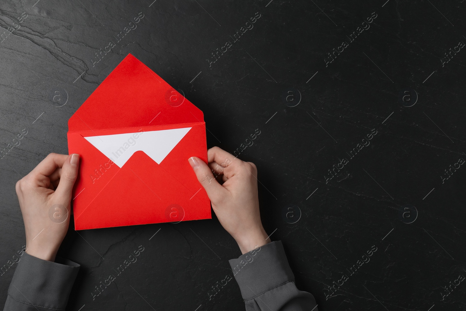 Photo of Woman holding letter envelope with card at black textured table, top view. Space for text