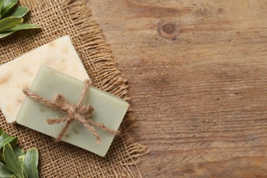 Photo of Soap bars and green plants on wooden table, flat lay. Space for text