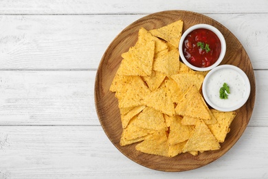 Photo of Plate with tasty Mexican nachos chips and sauces on white wooden table, top view. Space for text