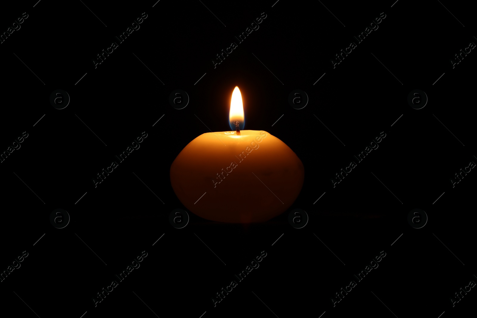 Photo of One burning wax candle on black background
