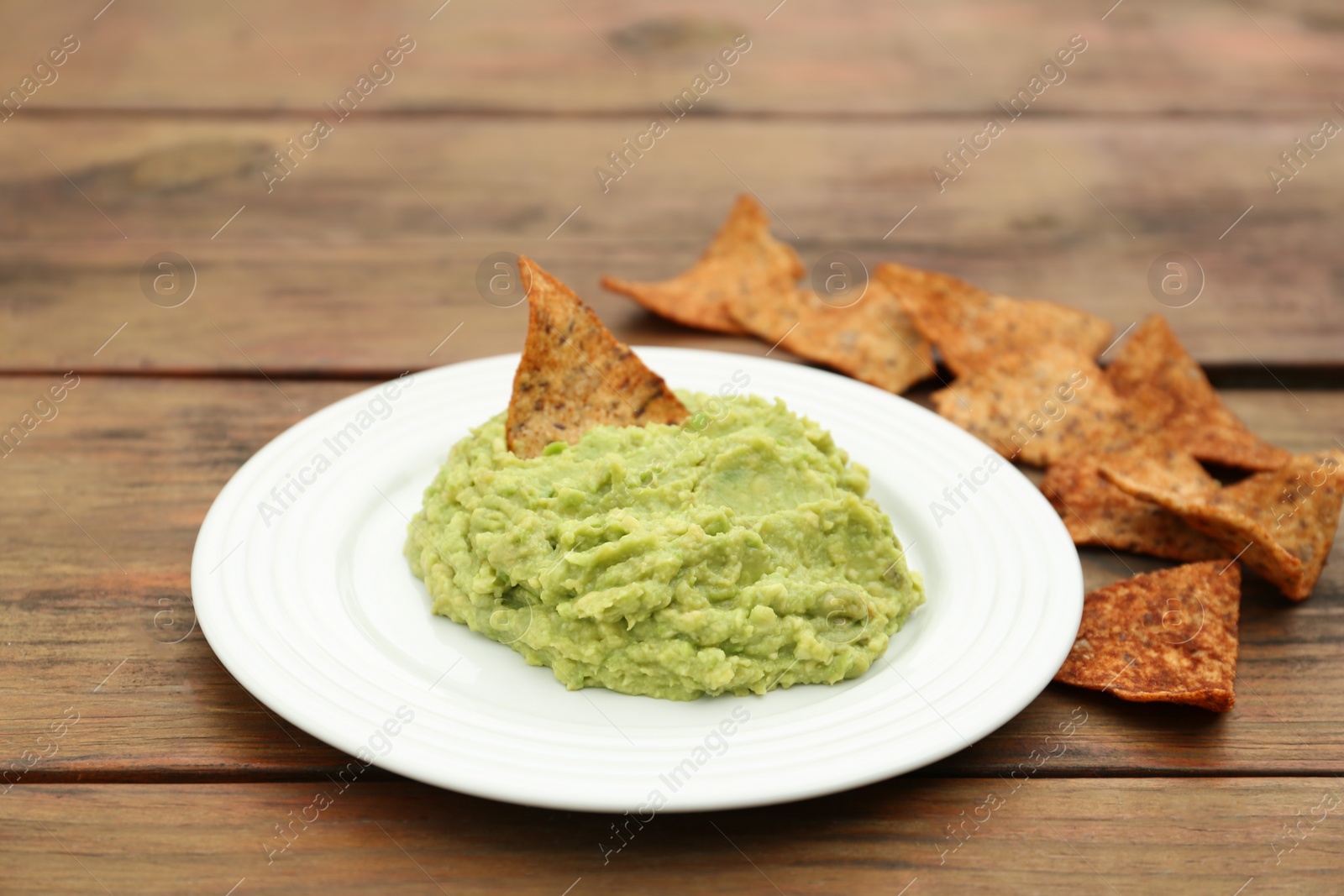 Photo of Delicious guacamole made of avocados and nachos on wooden table