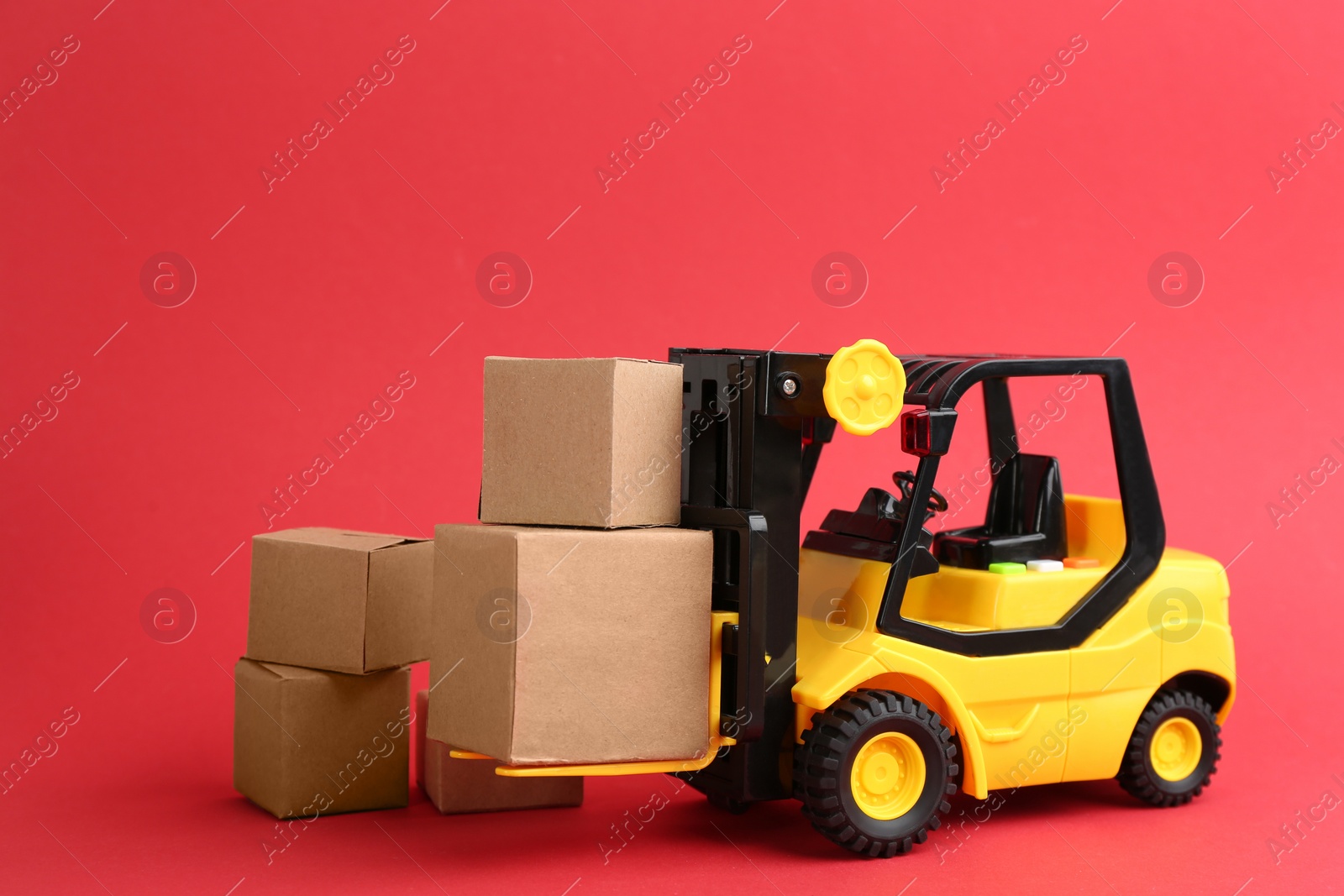 Photo of Forklift model and carton boxes on red background. Courier service