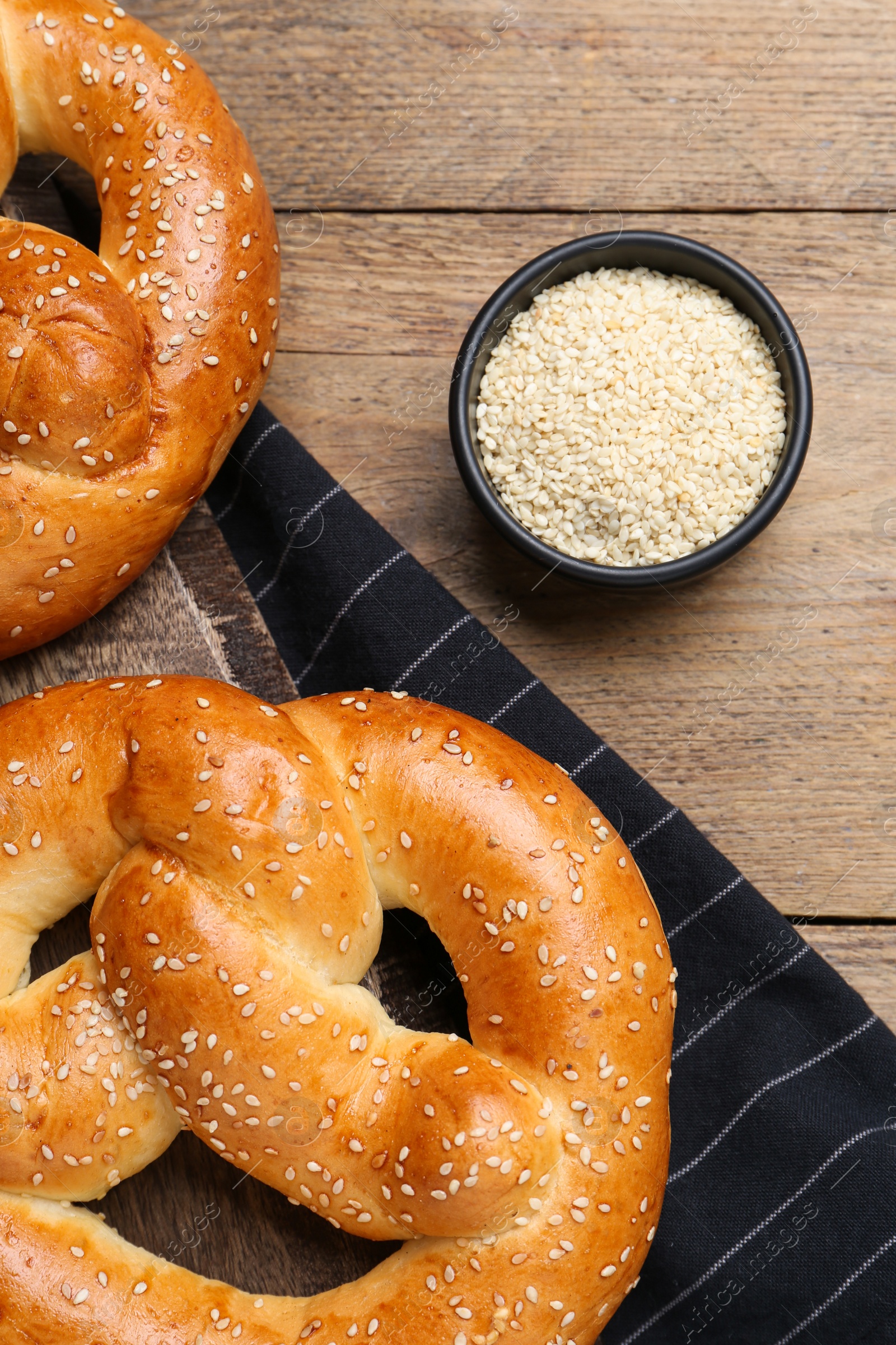 Photo of Delicious pretzels and bowl with sesame seeds on wooden table, flat lay