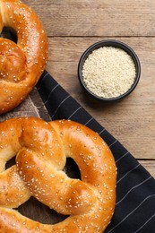 Delicious pretzels and bowl with sesame seeds on wooden table, flat lay